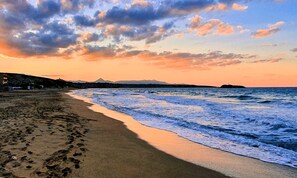 Una playa con huellas que conducen al agua, una montaña distante y un cielo al atardecer.
