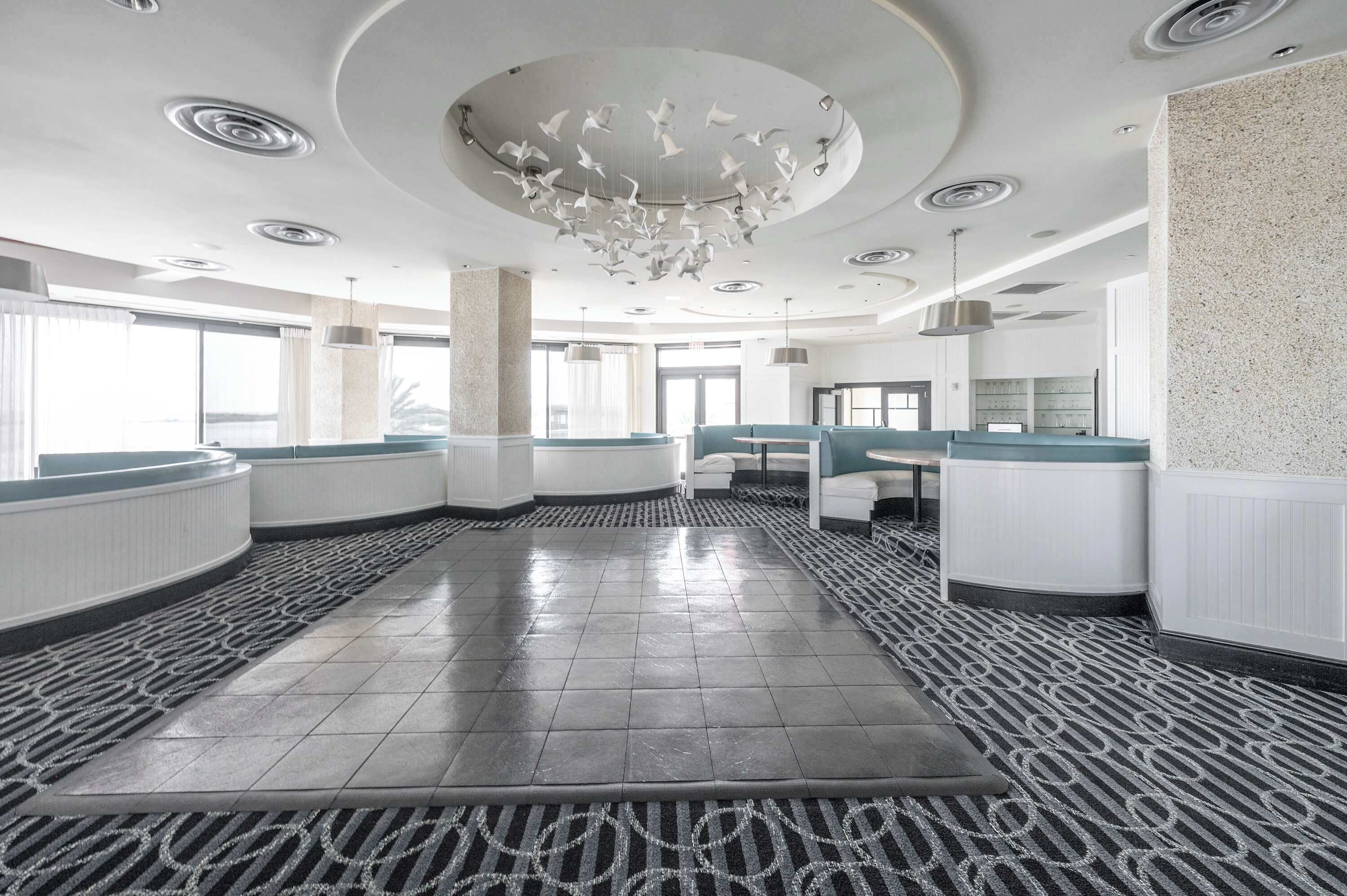 Un hall d’hôtel spacieux, doté d’un espace salon central, de grandes fenêtres et d’un sol à motifs.
