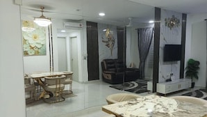 Uma sala de estar moderna com área de jantar, sofá, televisão e uma parede decorativa.