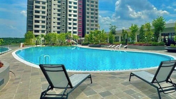 Piscina com espreguiçadeiras, cercada por um deck revestido em azulejos e um edifício residencial alto ao fundo.