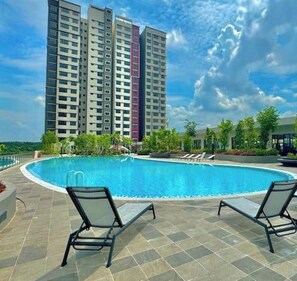 A swimming pool with lounge chairs, surrounded by a tiled deck and a tall residential building in the background. - HDIman Homestay Putrajaya KLIA view with Netflix Disney Sauna and Swimming Pool (Sepang)