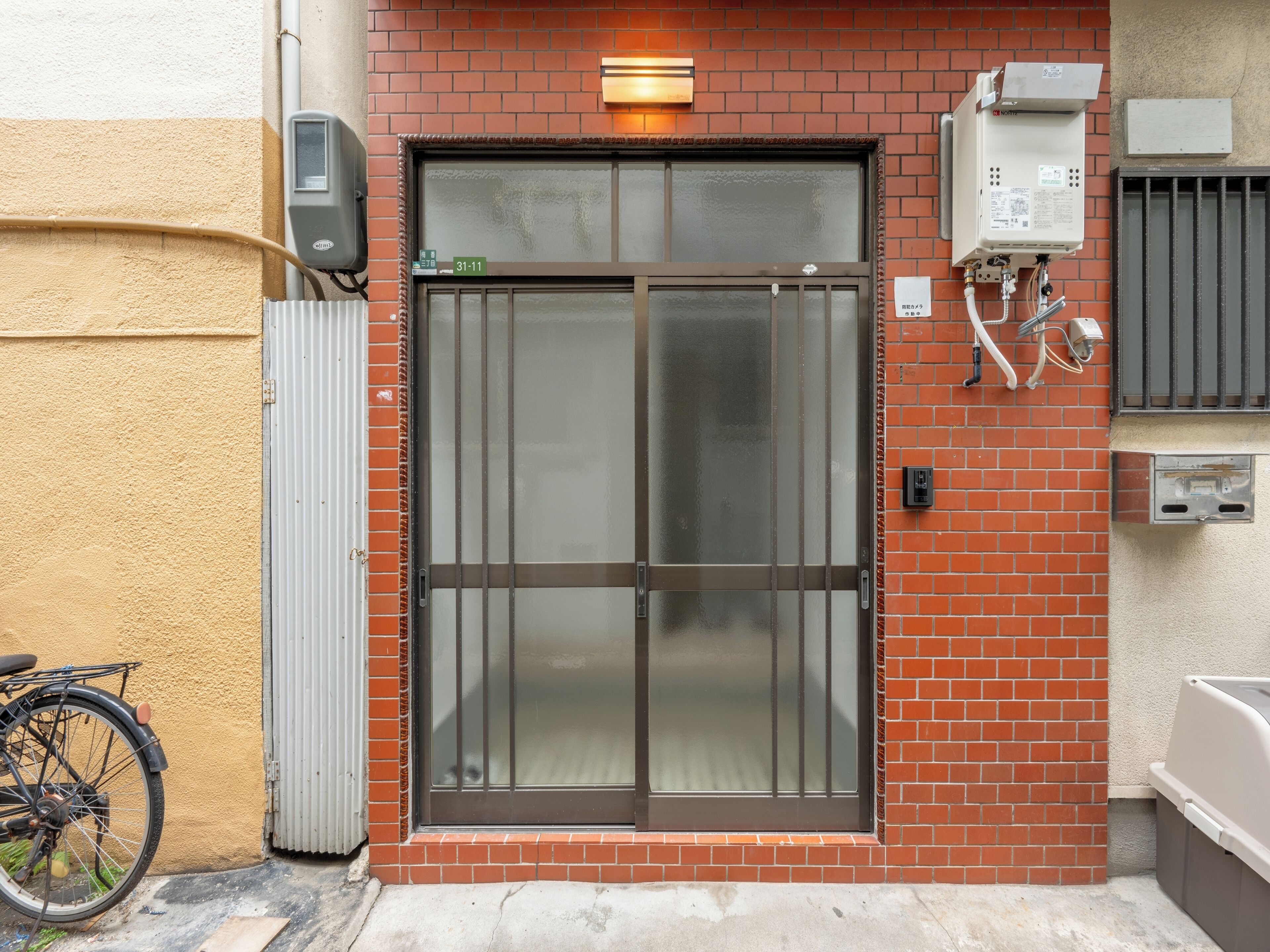 A building entrance with a glass door, a bike parked outside, and a utility box on the wall.