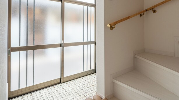 A modern interior with a glass door leading to a balcony, a wooden staircase, and a patterned floor.