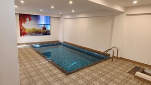 Une piscine avec un sol carrelé, une échelle en métal et un tableau accroché au mur.