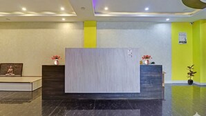 Un espace d’accueil avec un comptoir de réception, un tableau encadré sur le côté gauche et une plante en pot sur le côté droit.