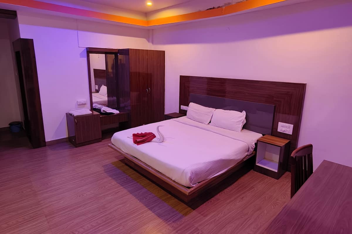 A modern hotel room with a large bed, wooden flooring, a wardrobe, and a bedside table.