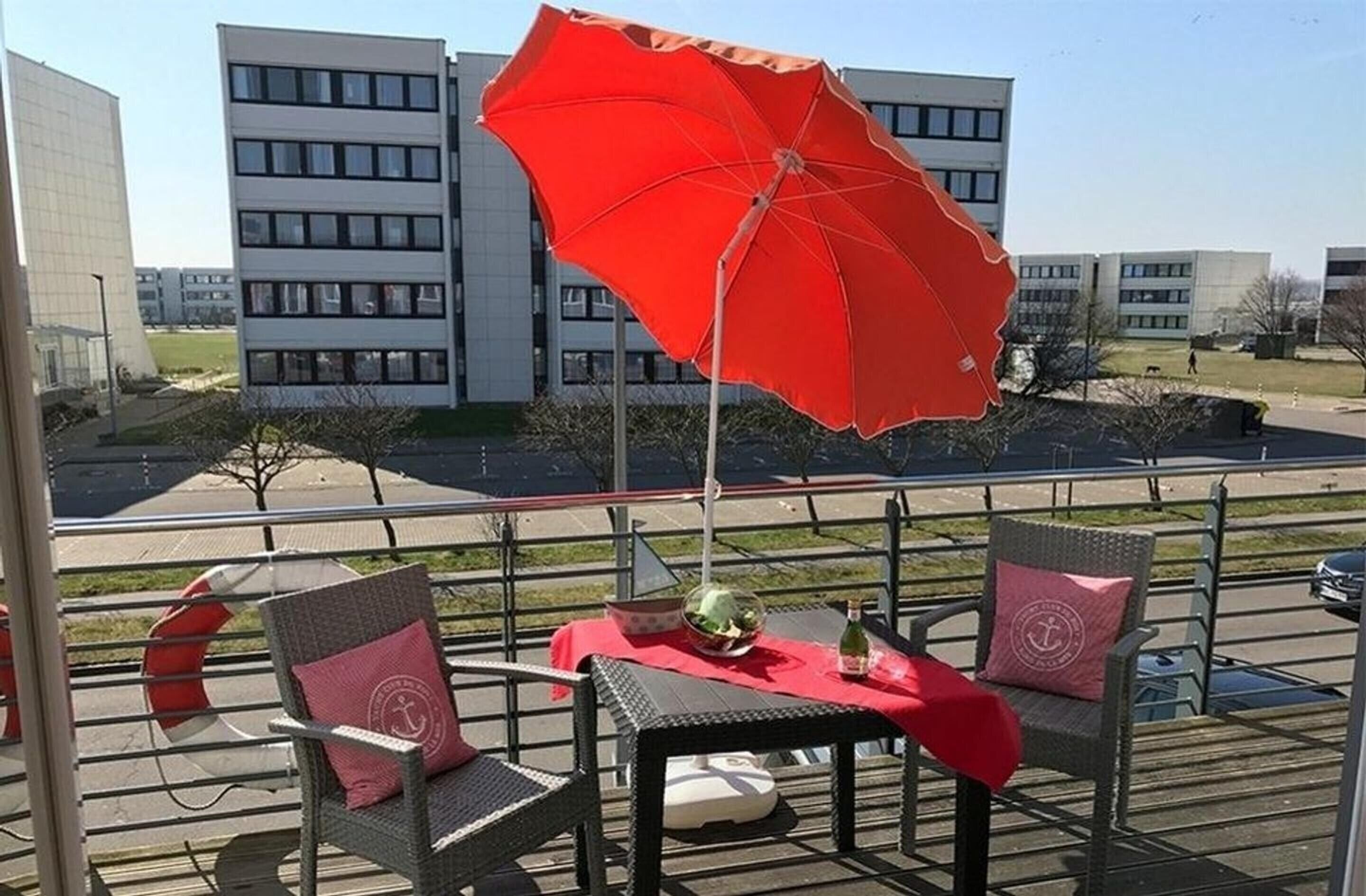 A balcony with wicker chairs, a table with a red tablecloth, and a red umbrella.