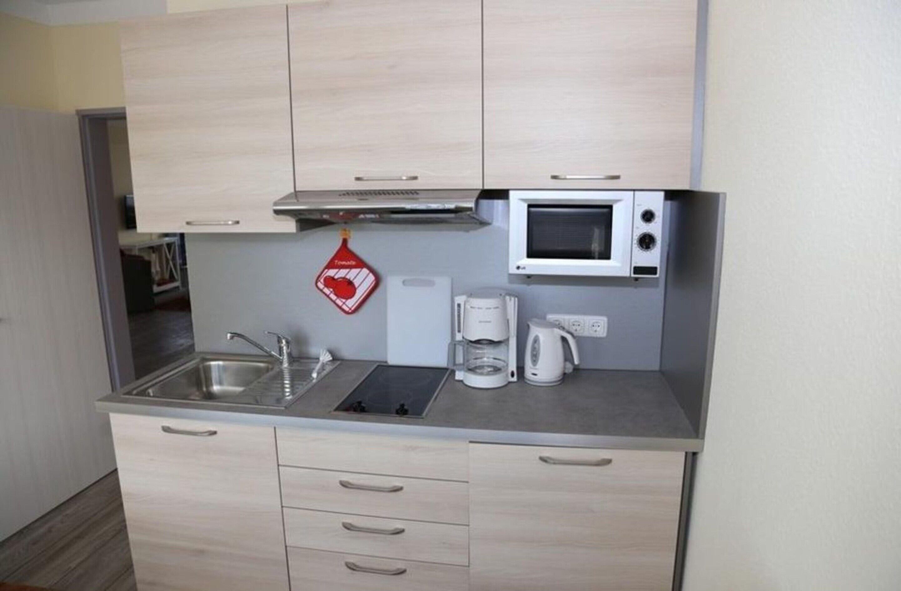 A compact kitchen with a microwave, coffee maker, and a red hanging pot holder.