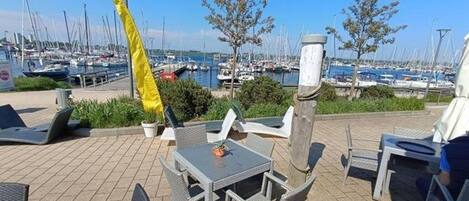 Patio exterior con mesas y sillas, con vistas a un puerto deportivo y barcos.