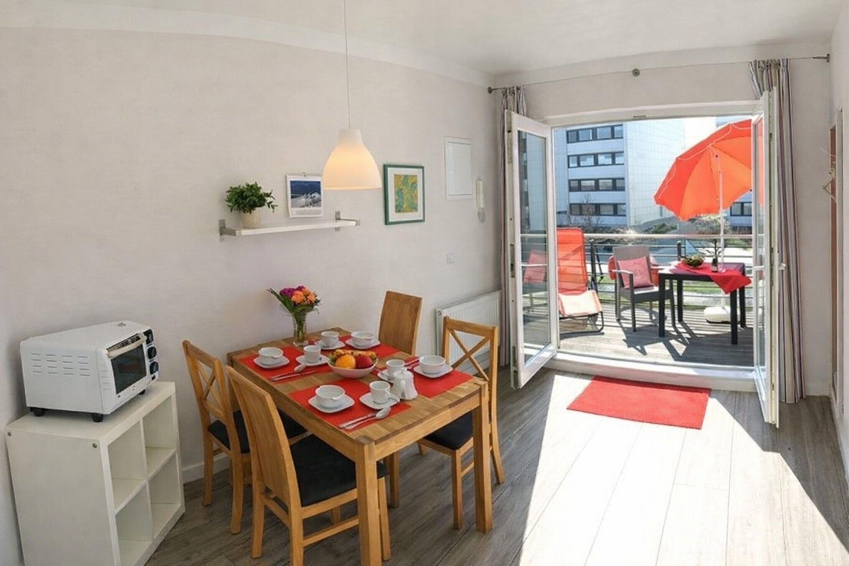 A dining area with a wooden table set for four, a microwave, and a small shelf with a plant.