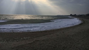 A beach with waves, a clear sky, and a distant building. - Apartment Am Sudstrand (Fehmarn)