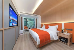 Quarto de hotel moderno com uma cama grande, uma TV na parede, uma mesa de cabeceira com abajur e uma janela com vista para árvores.