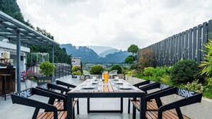 An outdoor dining area with a table and benches, surrounded by greenery and a view of mountains. - Zhangjiajie Yunxi Scenic Hotel (Zhangjiajie)