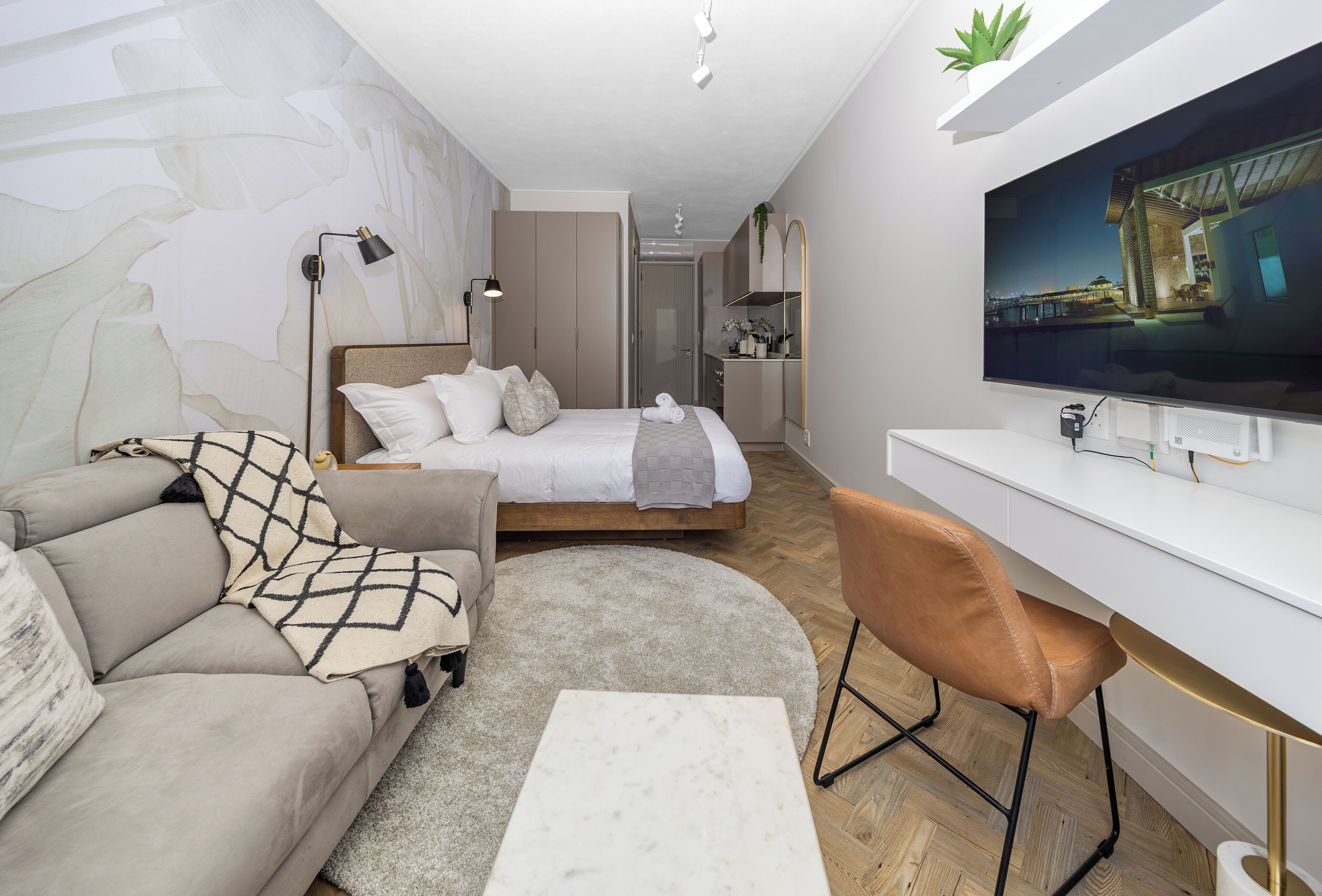 A modern bedroom with a bed, a sofa, a desk, and a TV.
