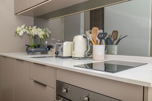 Eine moderne Küche mit weißer Arbeitsplatte, einem eingebauten Ofen, einem Toaster und einer Kaffeemaschine. Auf der Arbeitsplatte stehen Küchenutensilien in einem Behälter sowie eine Vase mit weißen Blumen.