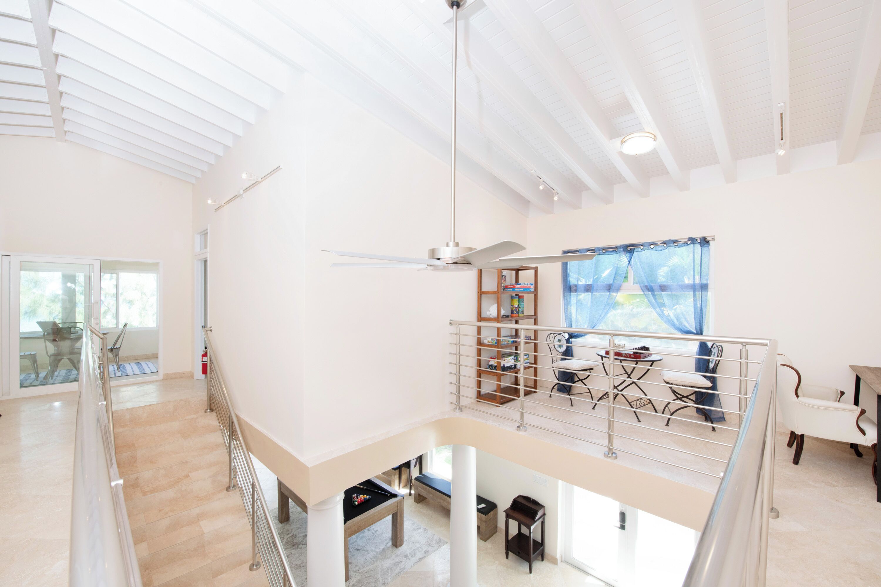 Una habitación amplia y luminosa con techo alto, ventilador de techo, balcón con barandilla y zona de comedor con mesa y sillas.