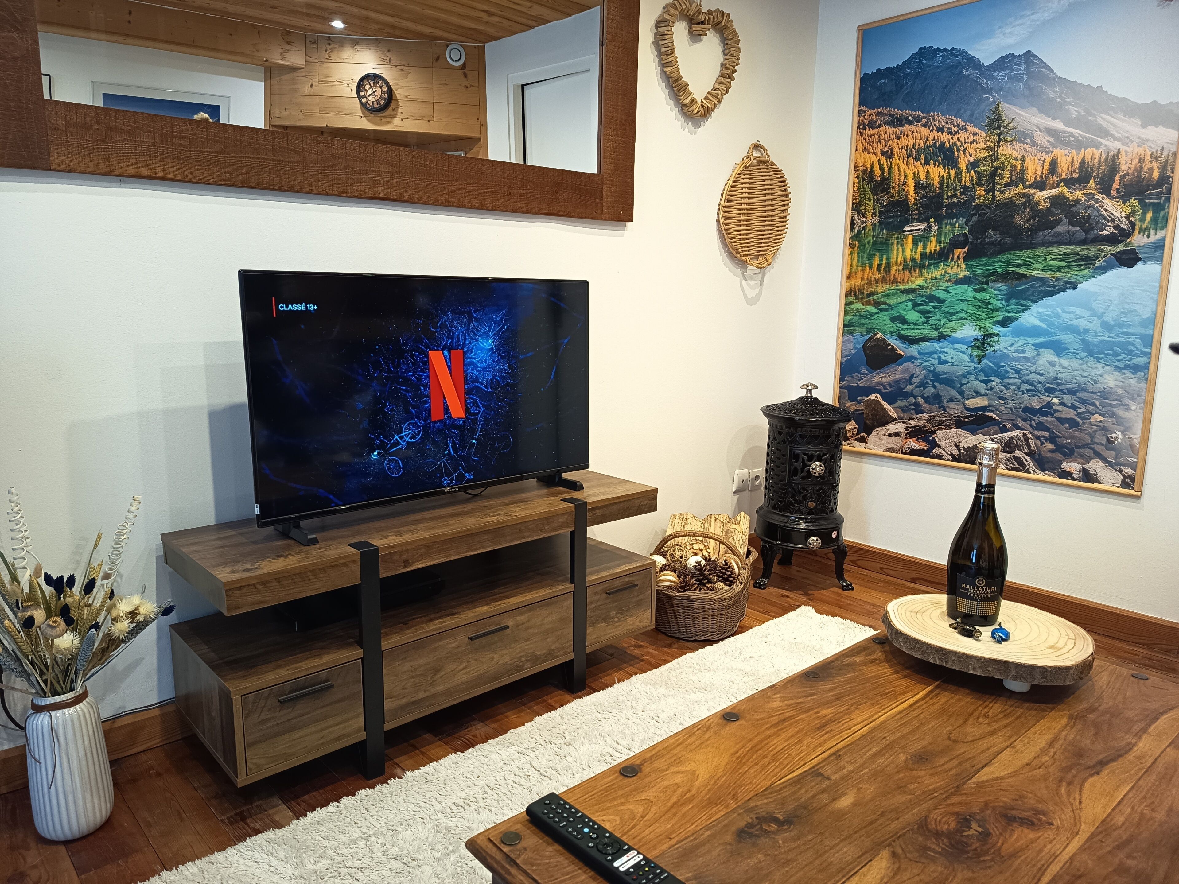 A modern living room with a flat-screen TV, wooden furniture, a decorative wall clock, a fireplace, and a scenic painting.