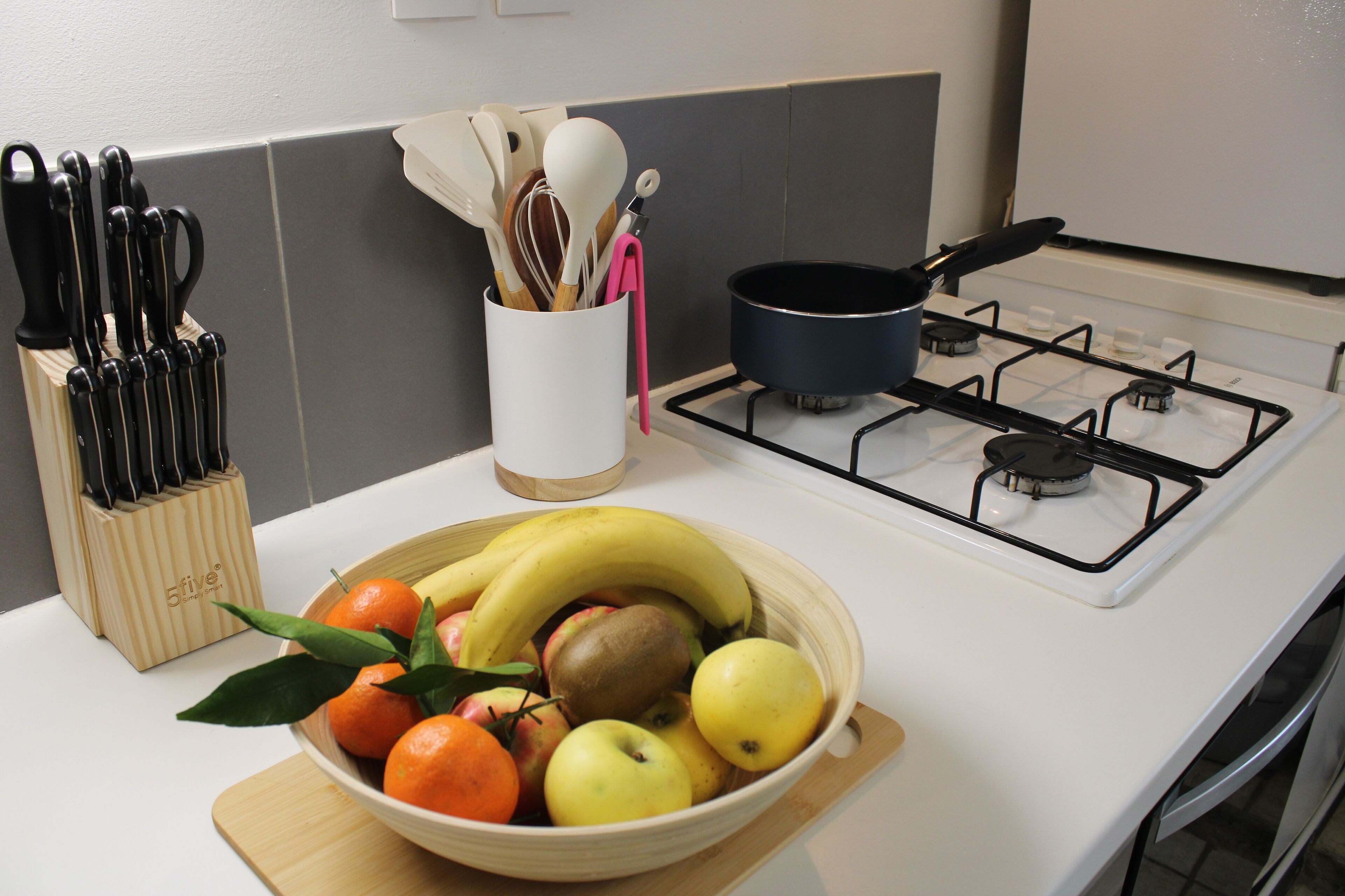 A kitchen with a gas stove, a bowl of fruit, and a knife block.
