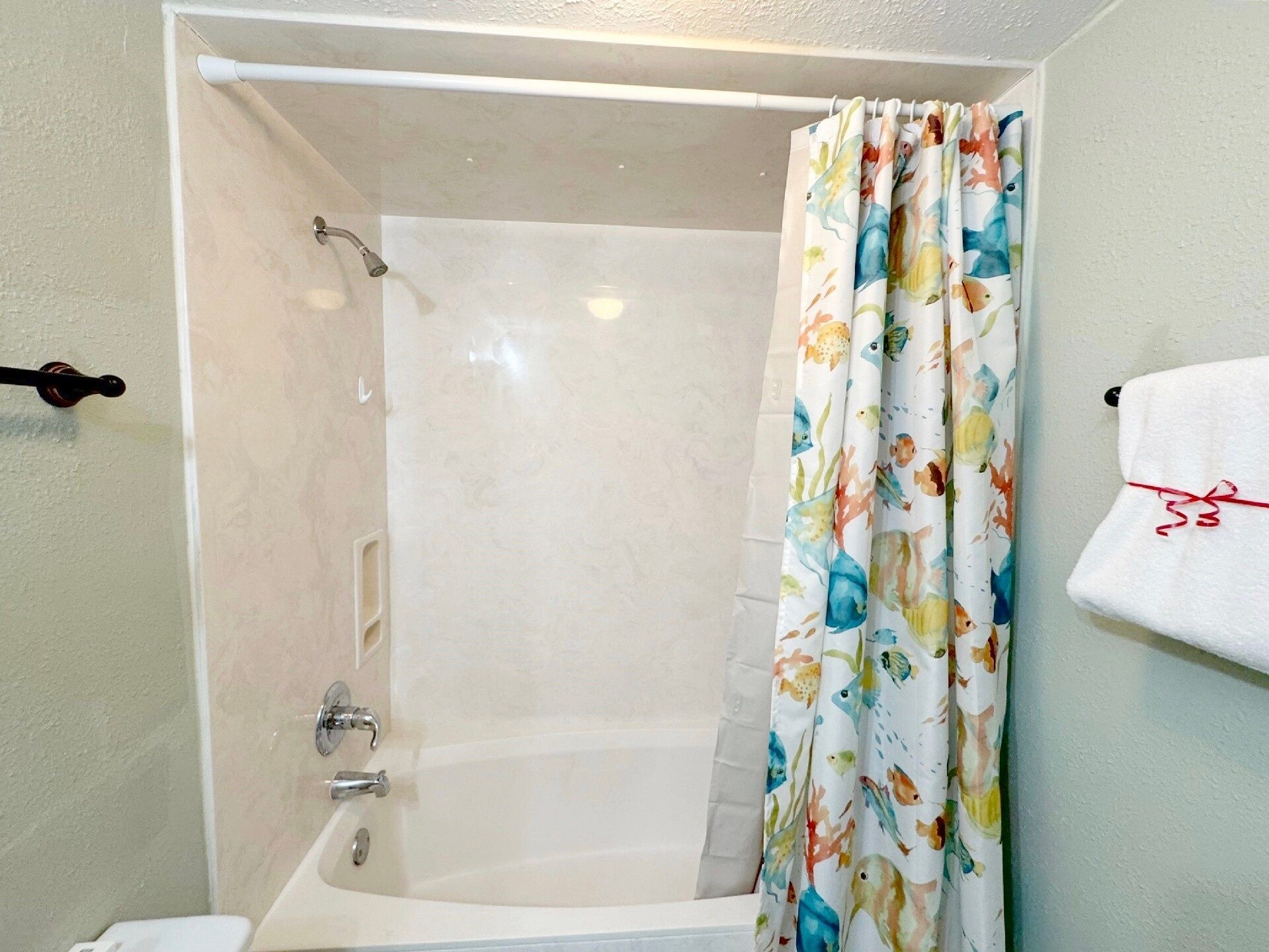 Un baño con una bañera, cortina de ducha con estampado de peces y un perchero con una toalla blanca.