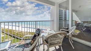 A balcony with wicker furniture, a glass table, and a view of the beach and ocean. - Shoreline Towers 2075 2 Bedroom Condo (Destin)