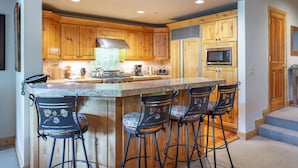 A kitchen with wooden cabinets, a large island with bar stools, a microwave, and a stove. - 503 - Four Bedroom with Spa Trail's End Lodge 4 Condo (Park City)