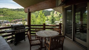 A covered outdoor area with a wooden table and chairs, a grill, and a view of a green landscape. - 503 - Four Bedroom with Spa Trail's End Lodge 4 Condo (Park City)