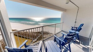Ein Balkon mit Blick auf Strand und Meer. Zwei blaue Adirondack-Stühle und ein kleiner Tisch sind vorhanden.
