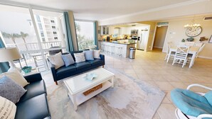 Ein modernes Wohnzimmer mit einer schwarzen Couch, einem weißen Couchtisch und Blick auf die Küche sowie den Balkon.