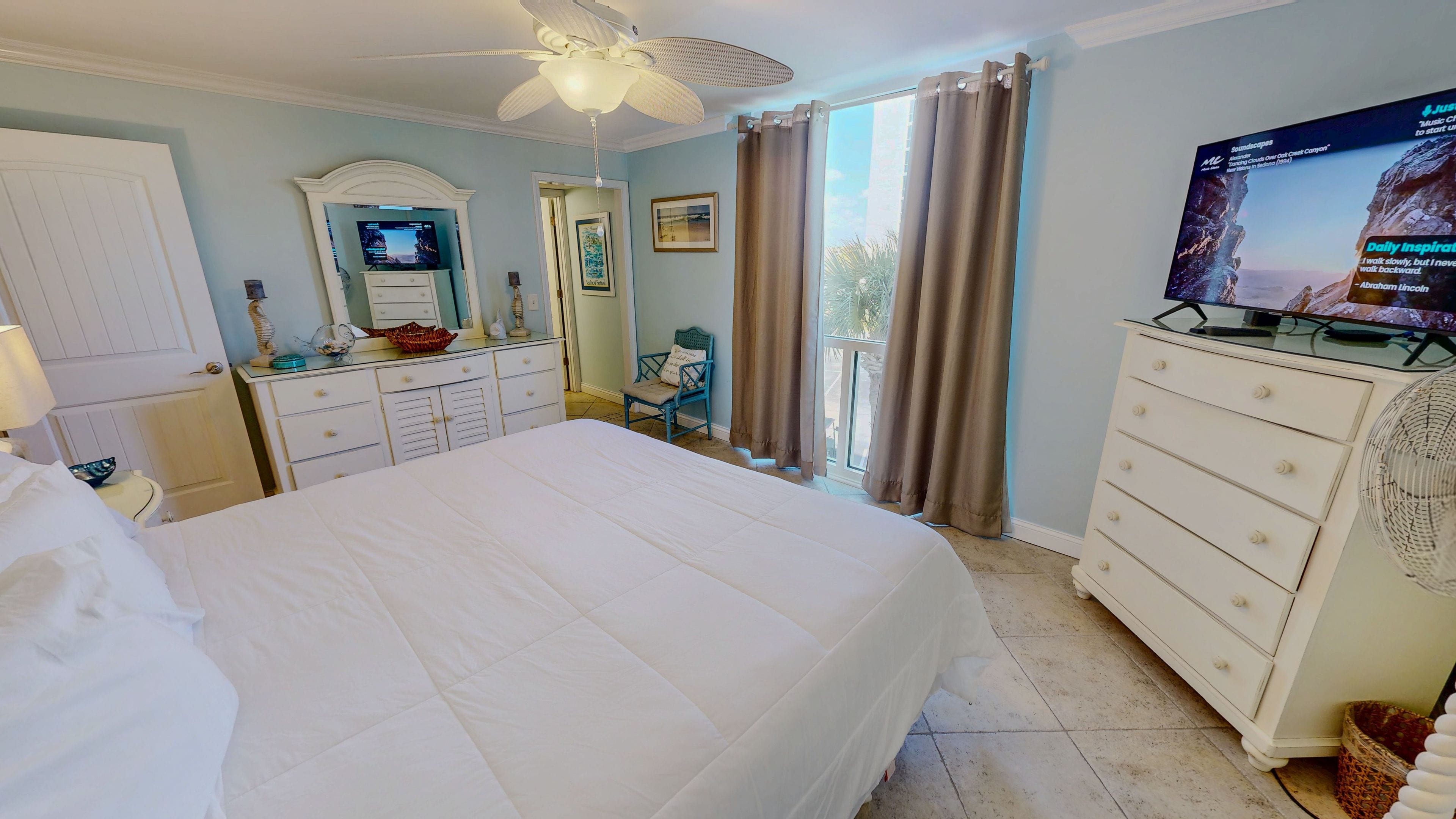 Habitación de hotel con una cama grande, televisión, ventilador de techo y vistas al exterior.
