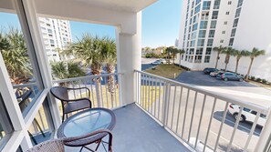 A balcony with wicker chairs and a glass table, overlooking a parking area and buildings. - Shoreline Towers 2031 3 Bedroom Condo (Destin)