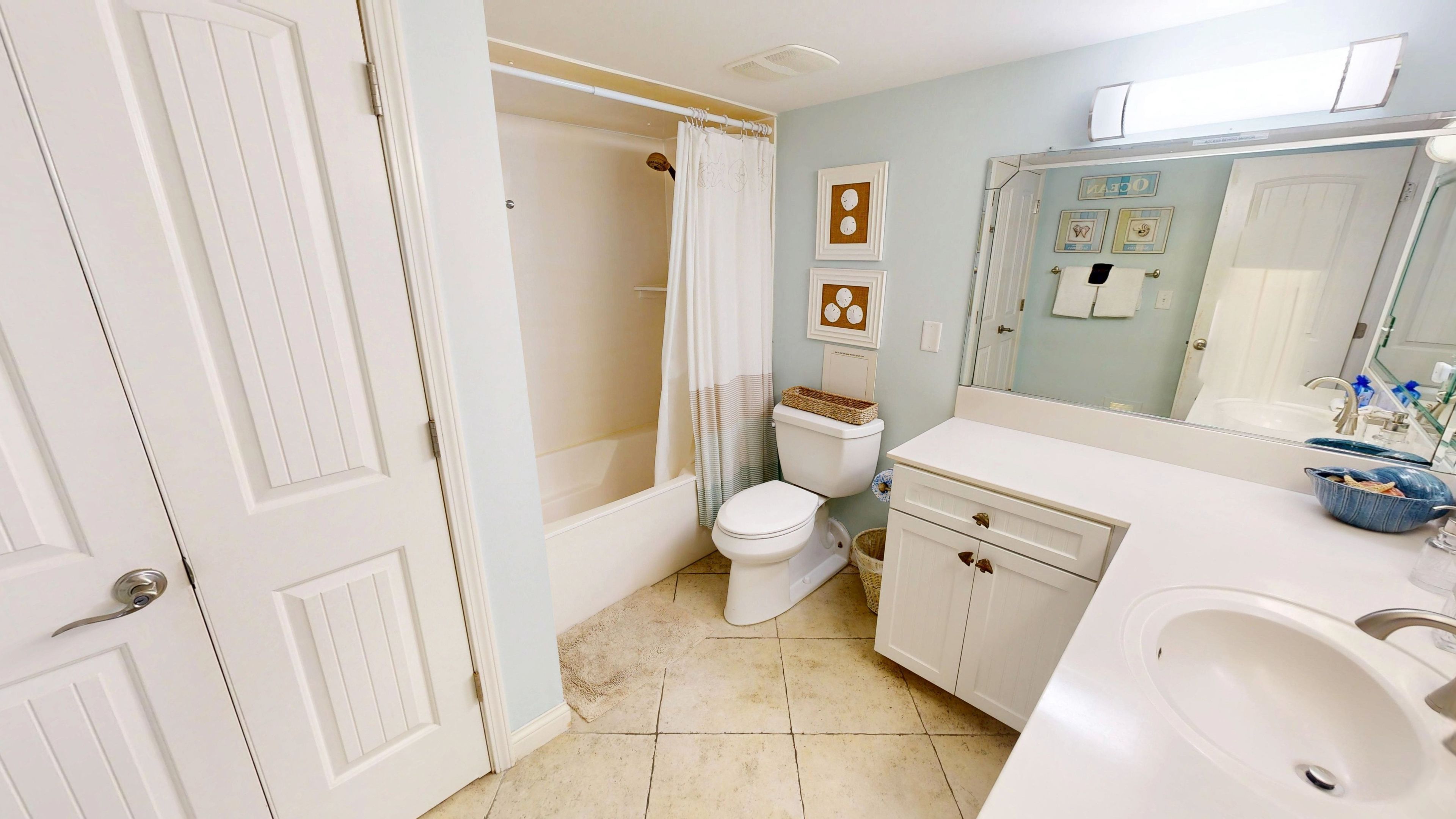 A bathroom with a bathtub, toilet, vanity, and a large mirror.