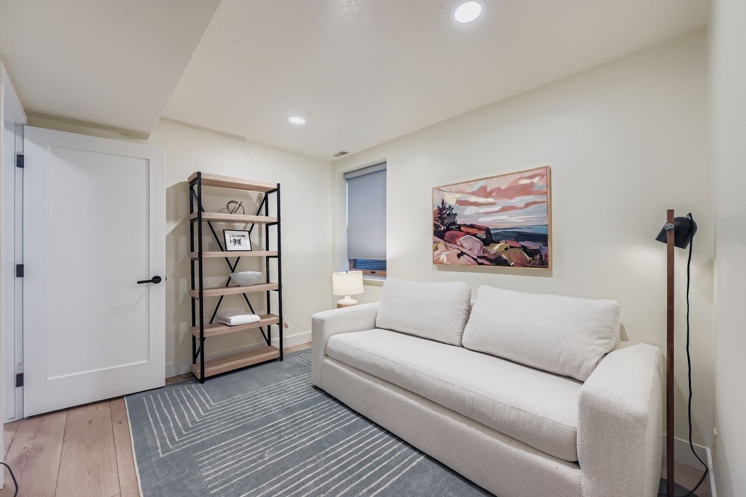 A living room with a white sofa, a wooden shelf unit, a painting, and a lamp.