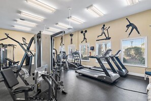 Un gimnasio con diverso equipamiento de ejercicio, incluyendo cintas de correr y máquinas de pesas, y amplias ventanas con persianas.
