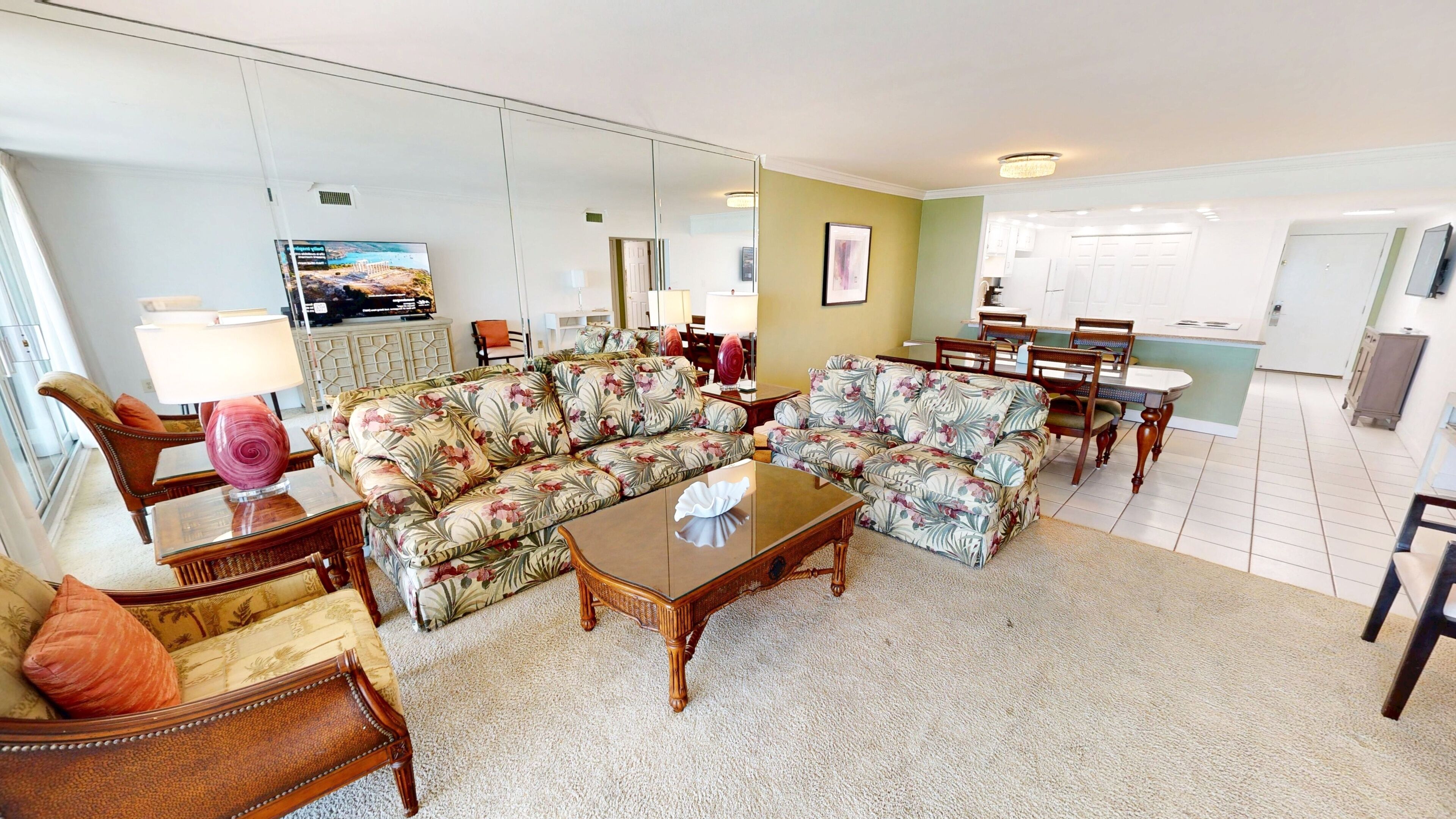 A spacious living room with a large floral sofa set, a coffee table, and a television.