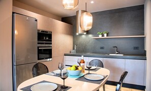 A modern kitchen with built-in appliances, a dining area with a table set for two, and a hanging pendant light. - Sissi Lux Triplex Villa Private Pools 36 Guests (Sisi)