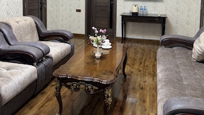 A room with a wooden coffee table, two sofas, a TV on the wall, and patterned wallpaper.