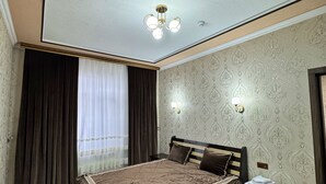 A bedroom with a large bed, a nightstand, a wall-mounted light, and a ceiling light fixture.