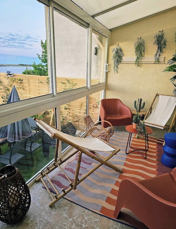 A balcony with a view of the beach, wicker furniture, and a cactus plant.