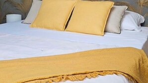 A bed with white bedding and two yellow pillows, a white bedside table, and a yellow throw blanket.