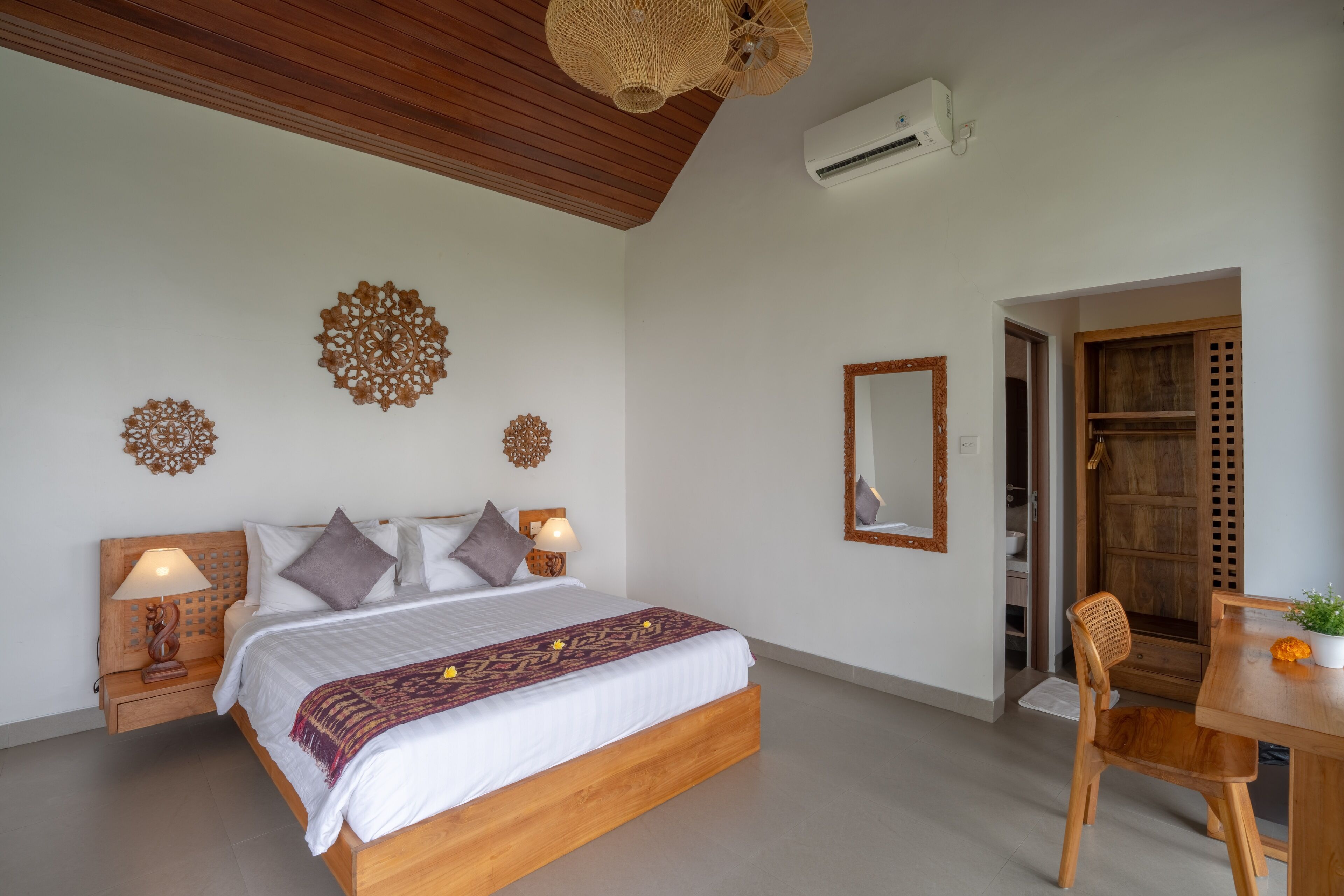 Une chambre avec un lit en bois, deux tables de chevet avec des lampes, une chaise en bois, une table à manger avec une plante en pot et un miroir au mur.