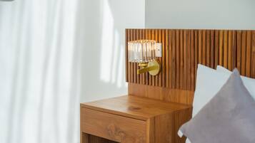 Uma mesa de cabeceira de madeira com uma gaveta, um candeeiro fixado na parede e uma cama com almofadas.