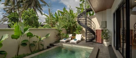 A swimming pool with lounge chairs, surrounded by tropical plants and a spiral staircase.