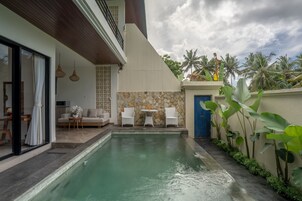 Una casa moderna con piscina, un patio con sillas blancas y un muro de piedra.