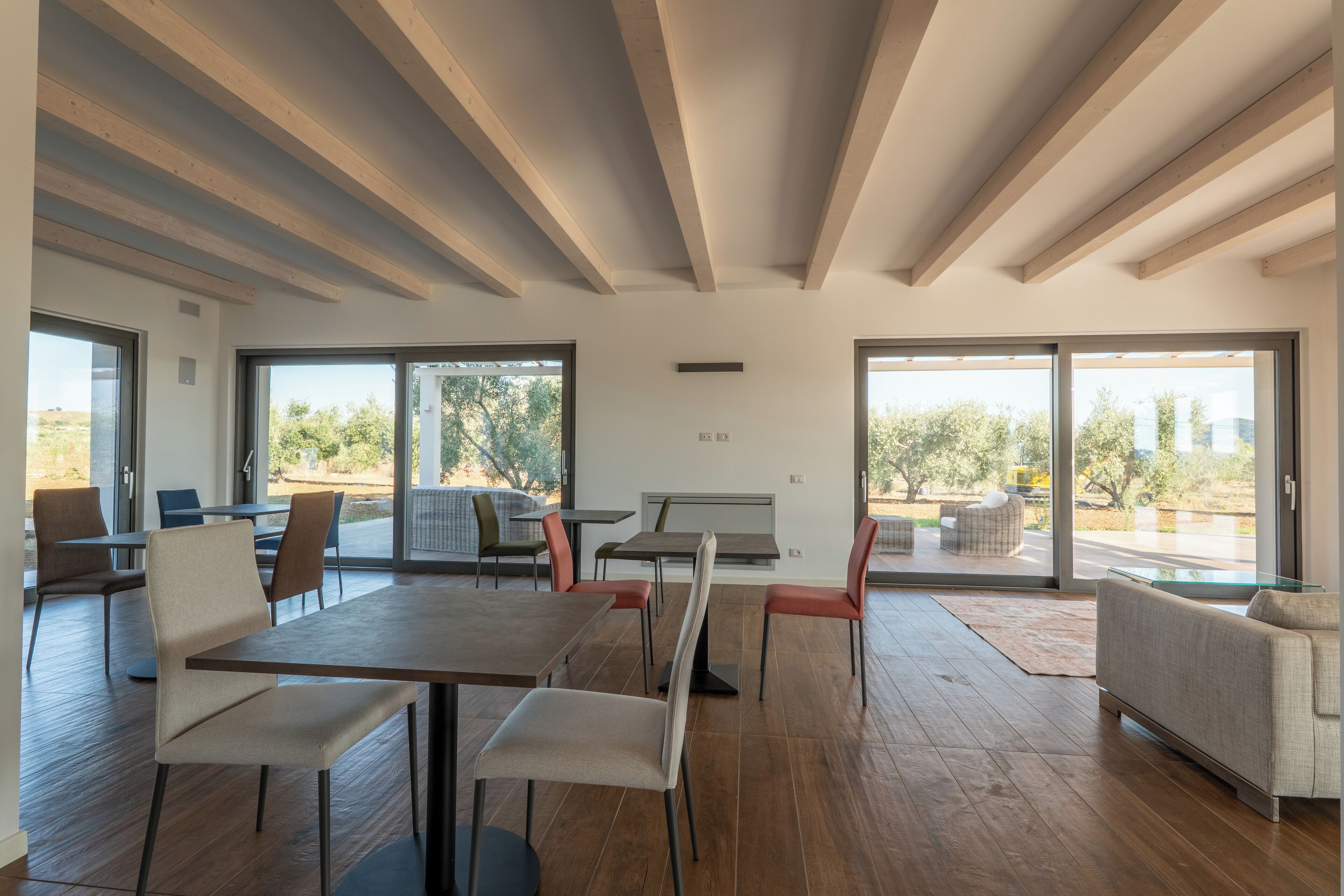 A modern dining area with wooden beams, large windows, and a view of the outdoors.