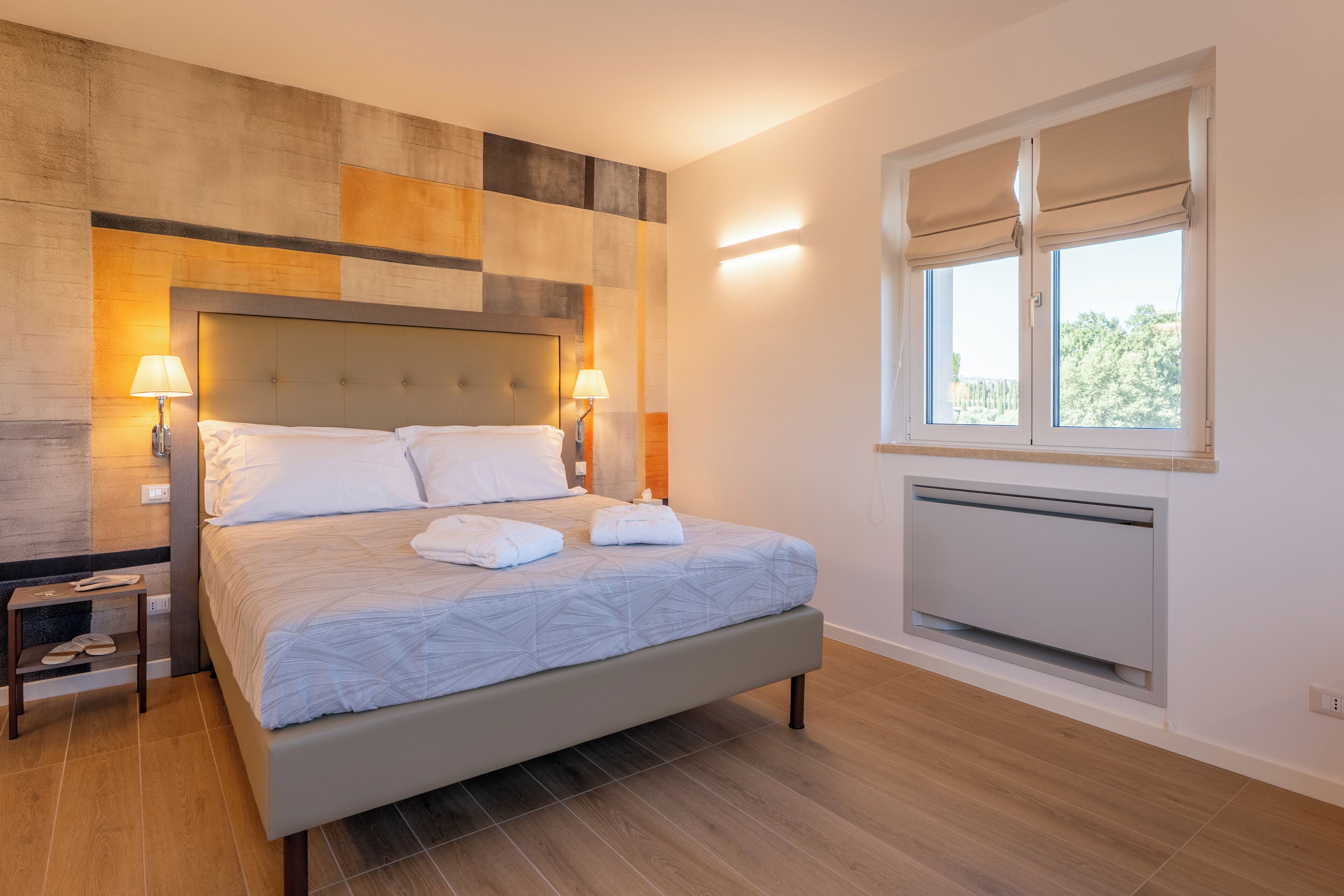 Quarto moderno com cama grande, abajures, janela com persianas e radiador.
