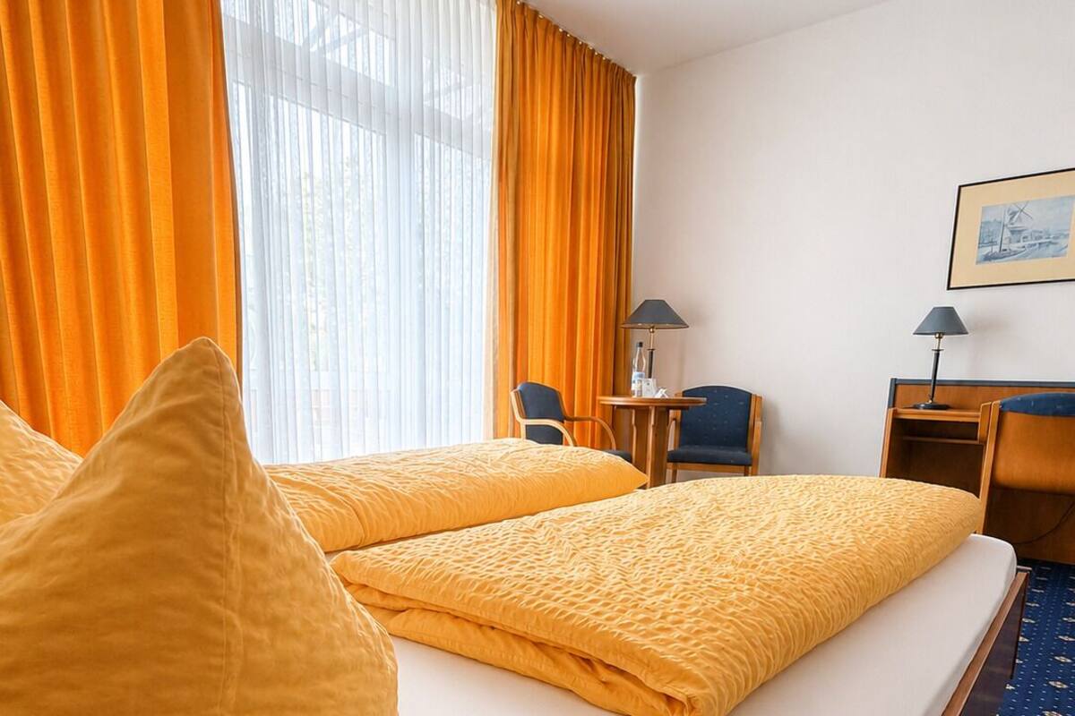 A hotel room with two beds, a desk, a chair, a lamp, and a framed picture on the wall.