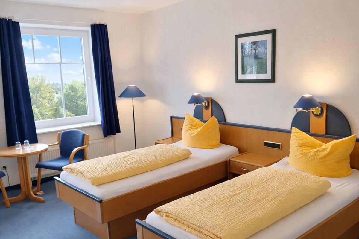 A hotel room with two beds, a desk, a chair, and a window with curtains.