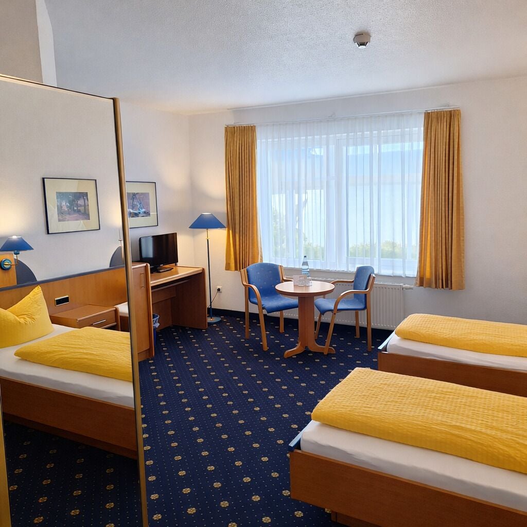 Een hotelkamer met twee bedden, een bureau met stoel, een televisie en een raam met gordijnen.