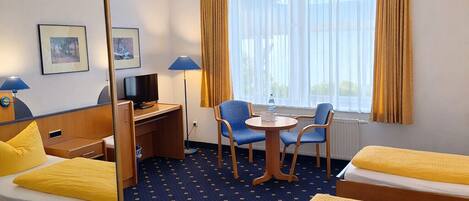 A hotel room with two beds, a desk with a chair, a TV, and a window with curtains.