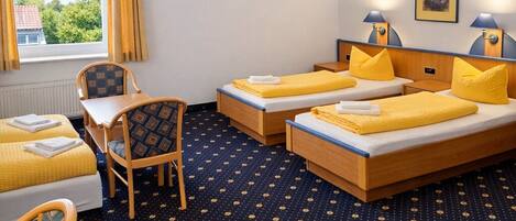 Quarto de hotel com duas camas, uma escrivaninha, uma cadeira e uma janela com cortinas.